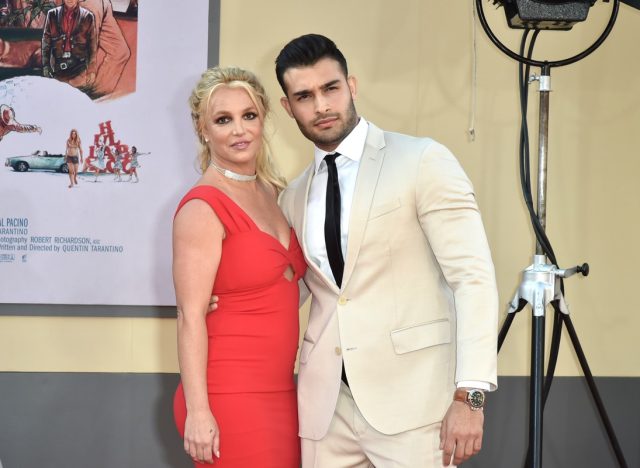 sam asghari in a tan suit standing next to britney spears in red dress on red carpet