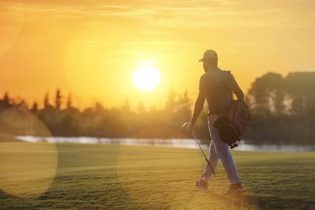 golfer carrying bag and walking to next hole at golf course on beautiful sunset in background