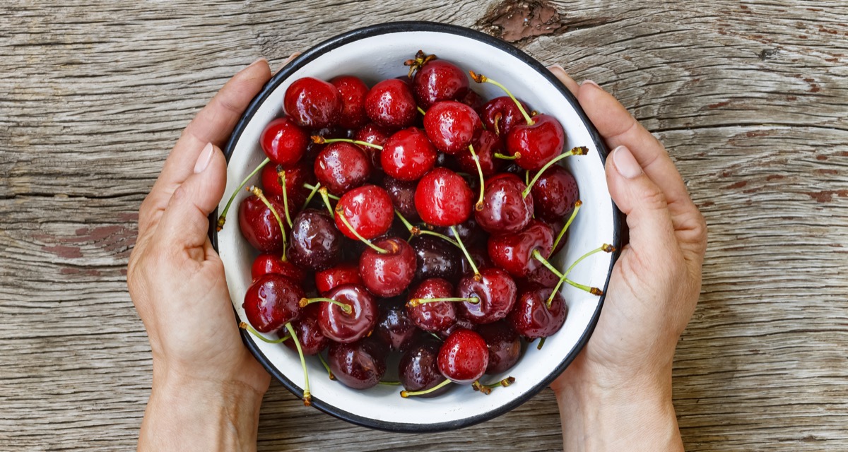 two hands holding white bowl of cherries