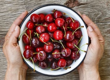 two hands holding white bowl of cherries
