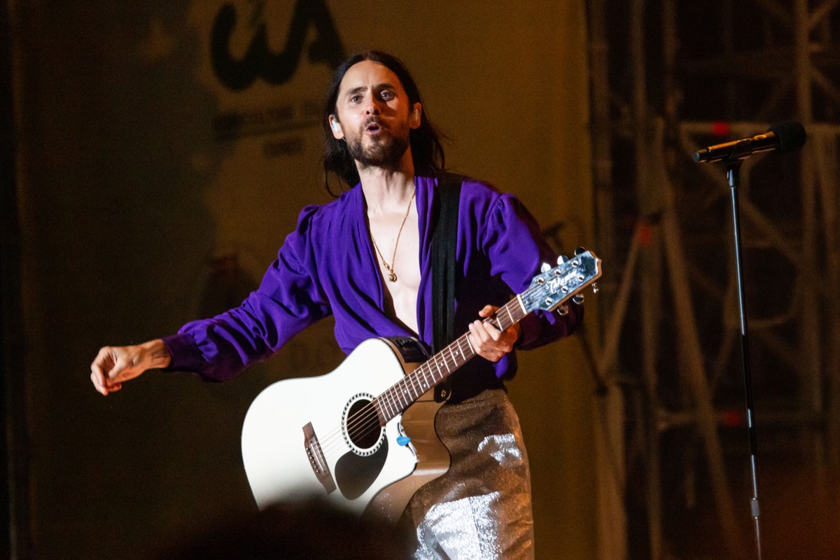 jared leto playing guitar in purple shirt and white pants