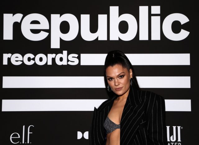 jessie j in high ponytail and gray crop top in front of black and white republic records flag