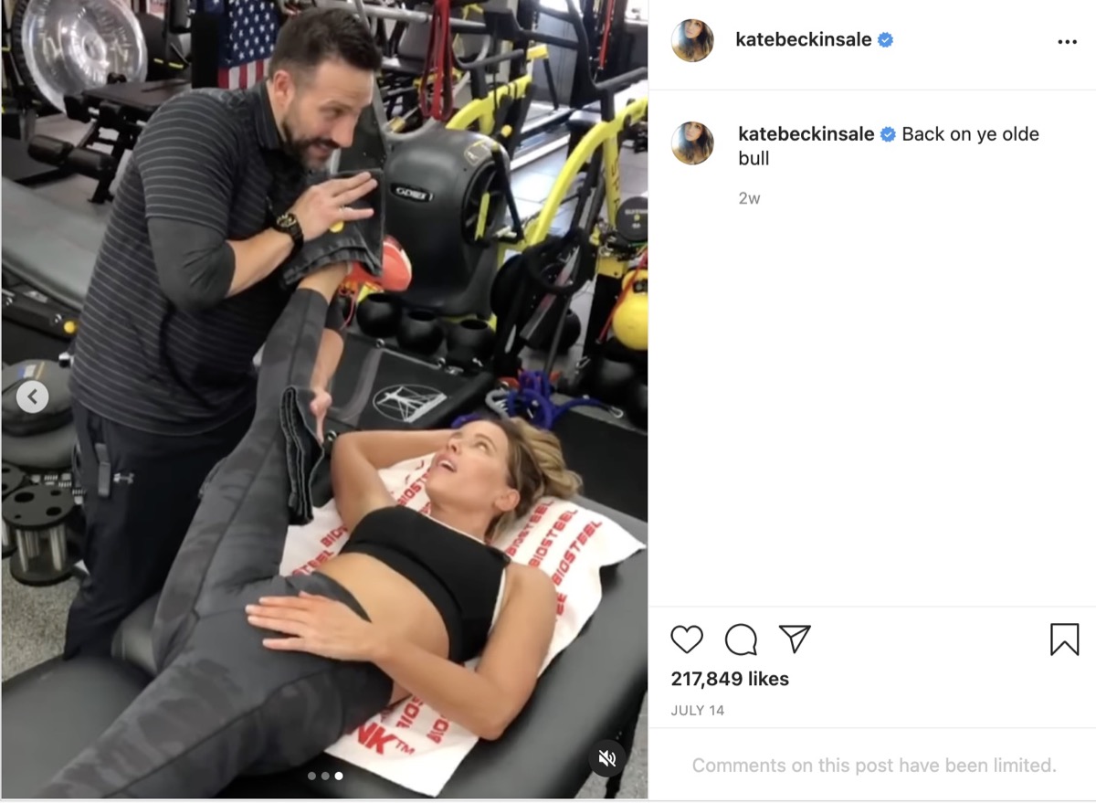 screenshot of male trainer stretching kate beckinsale's leg toward her head on instagram