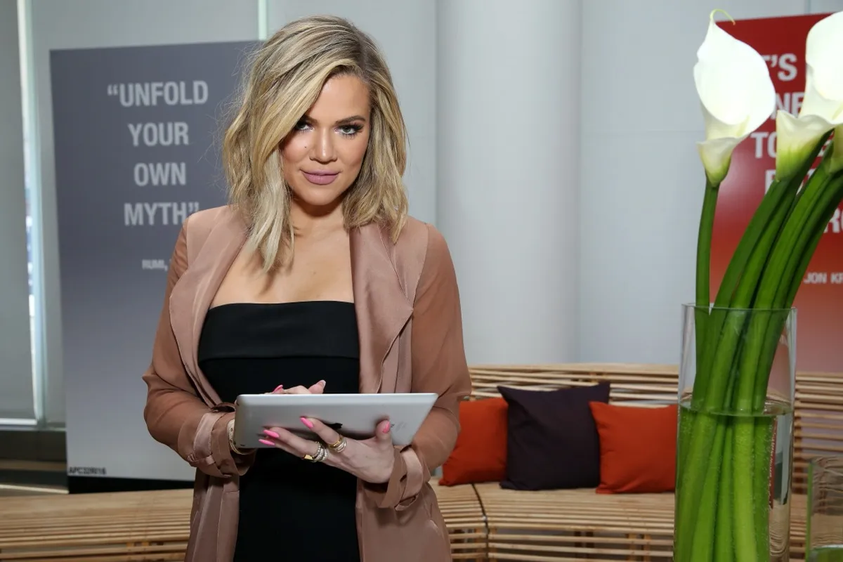 khloe kardashian in pink jacket and black top holding ipad