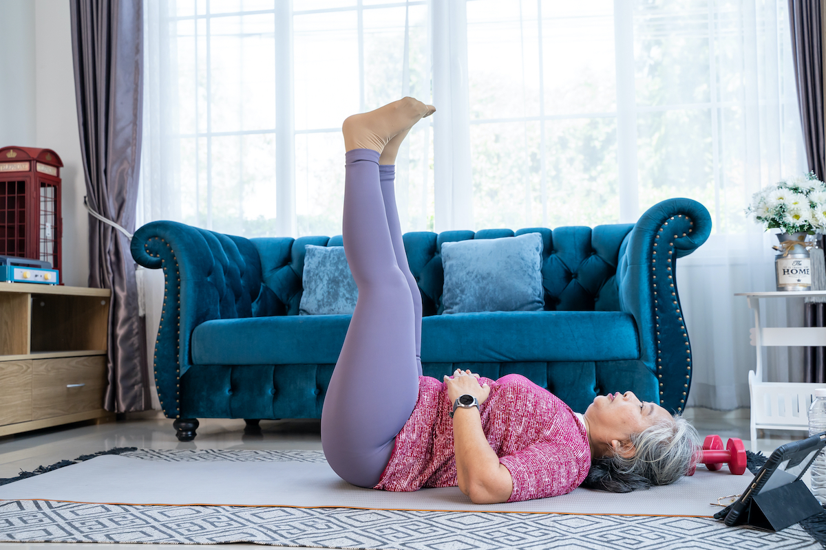Healthy Senior woman lie on the floor and raise two leg up while doing exercise stretching legs with lying leg lift, workout fitness pose at home