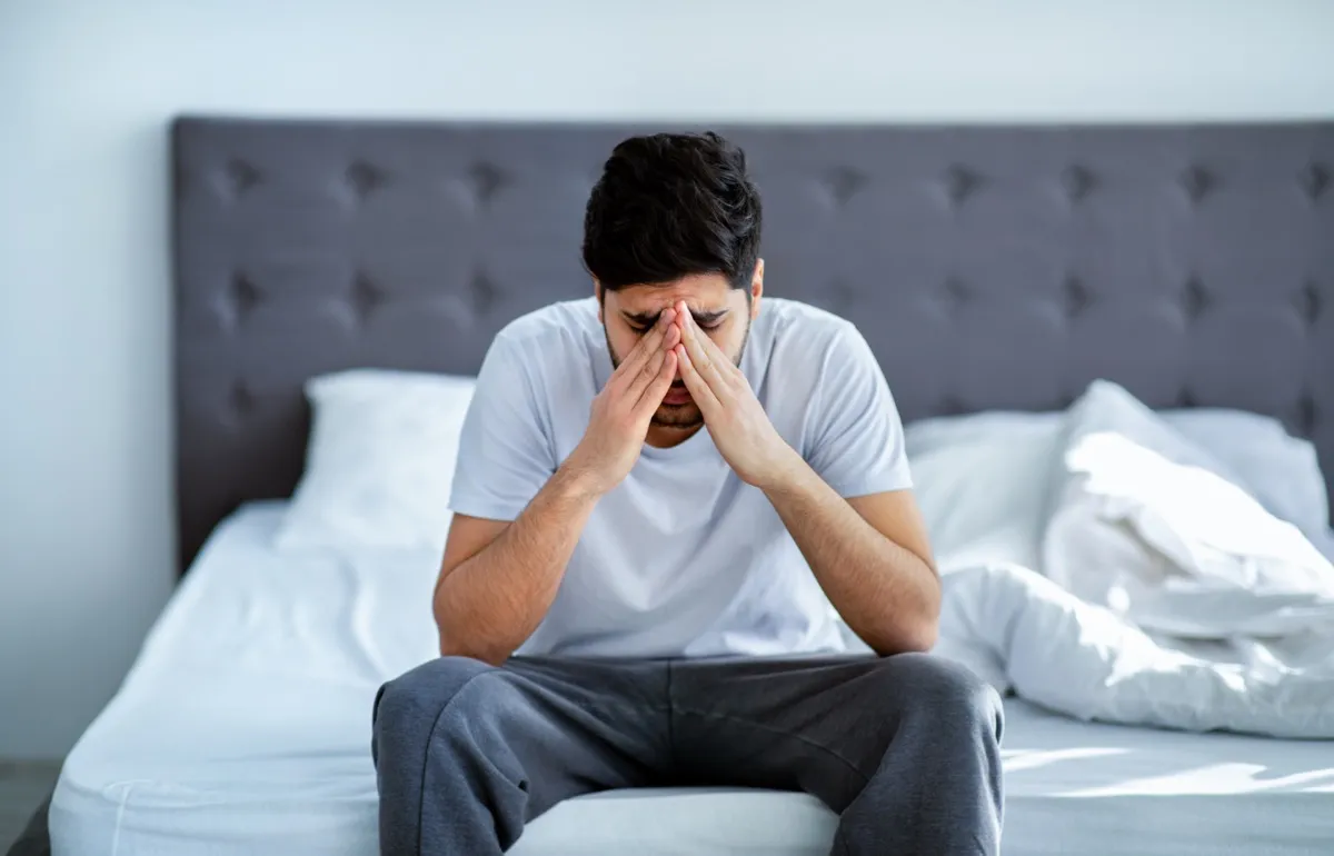 Man sitting on bed holding his head.