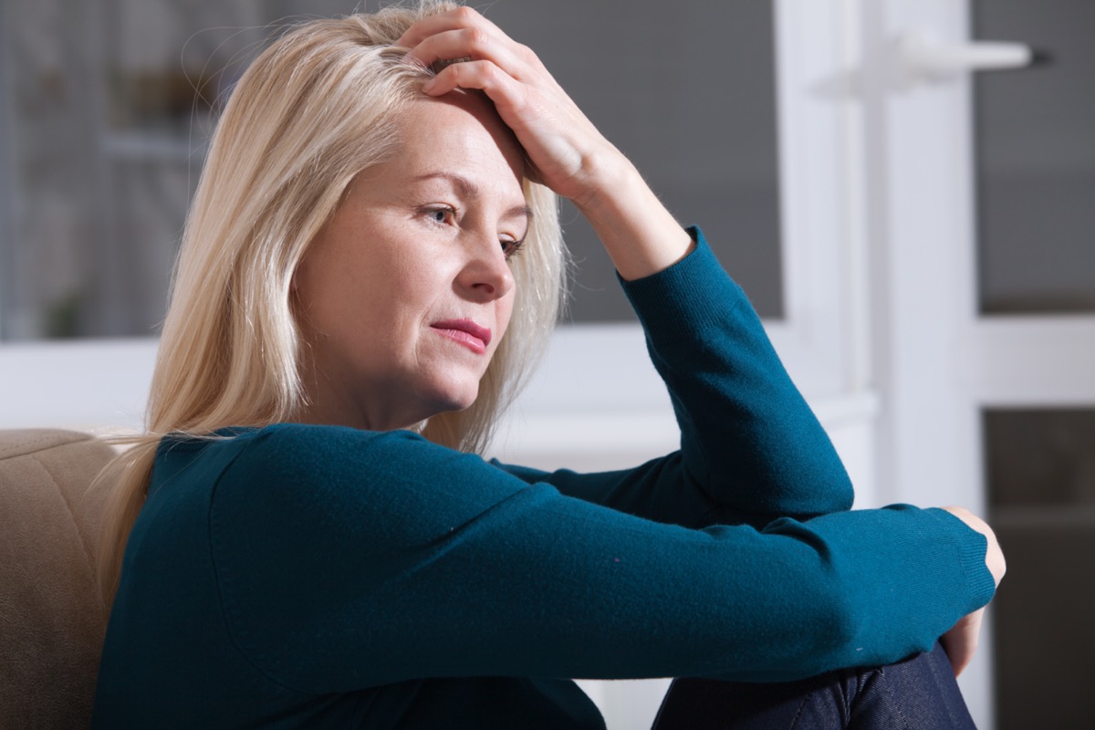 Sad depressed woman at home sitting on the couch, looking down and touching her forehead.