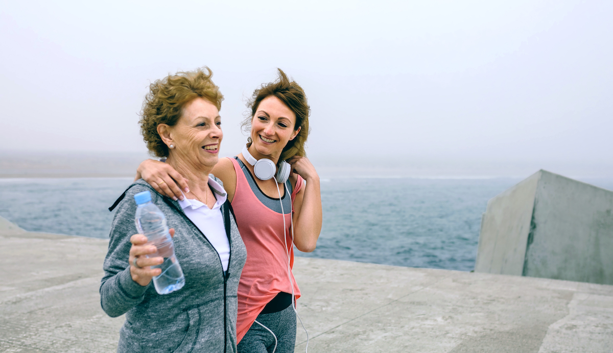 Senior woman and young woman walking outdoors by sea pier