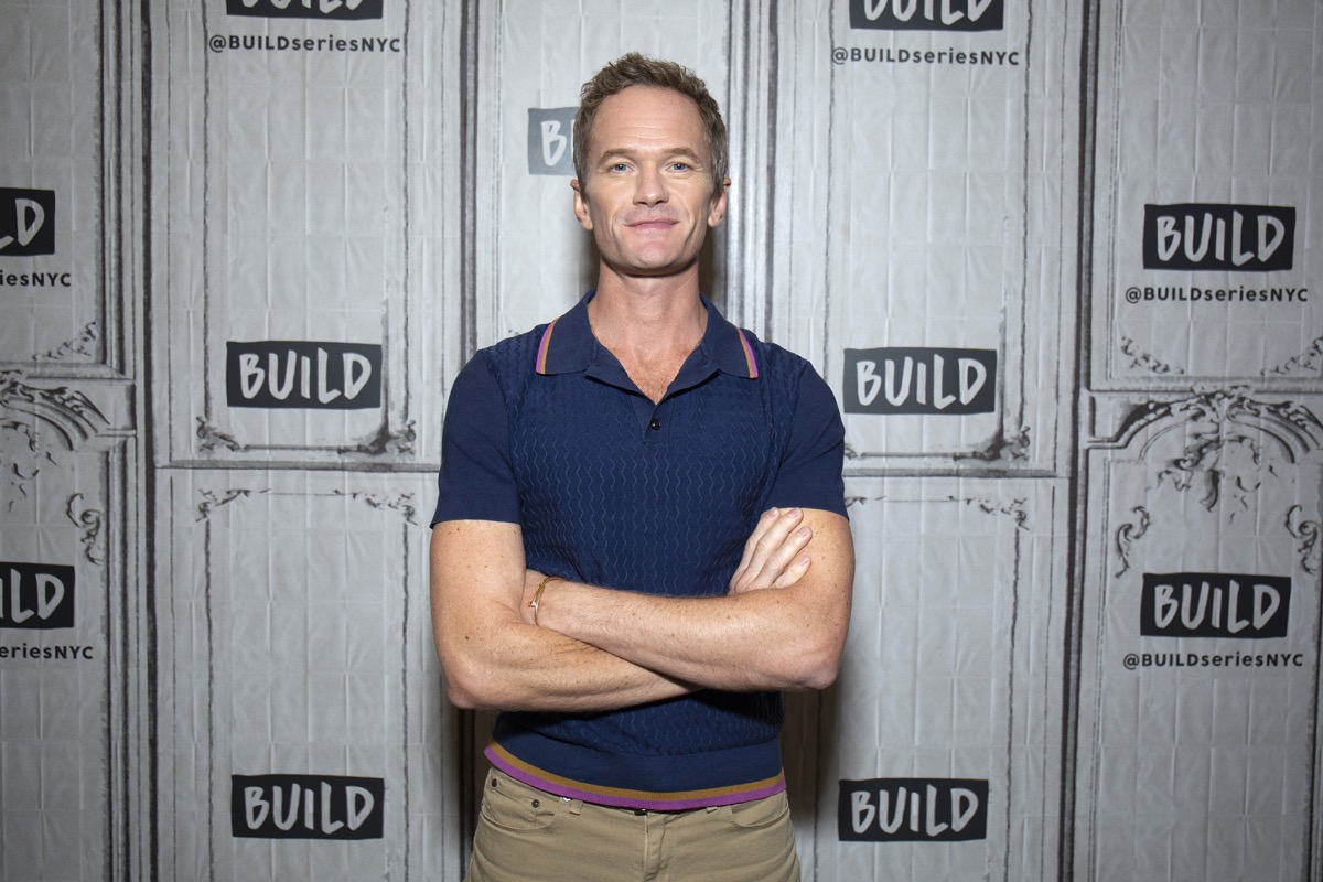 neil patrick harris with arms crossed wearing blue polo shirt in front of build studios step and repeat