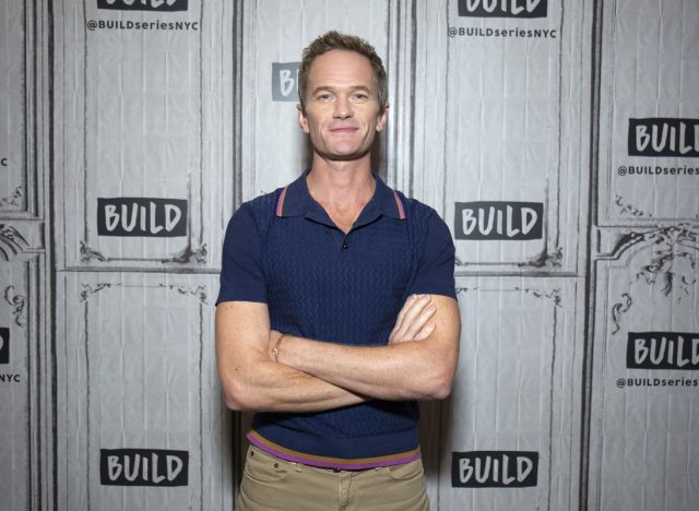neil patrick harris with arms crossed wearing blue polo shirt in front of build studios step and repeat