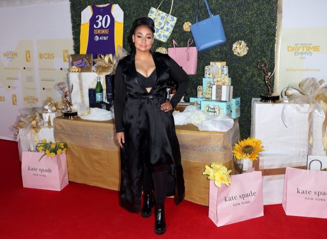 raven-symone in long black satin dress or cape in front of gifting suite and pink kate spade bags
