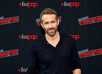 ryan reynolds in black unbuttoned henley in front of ny comic-con step and repeat