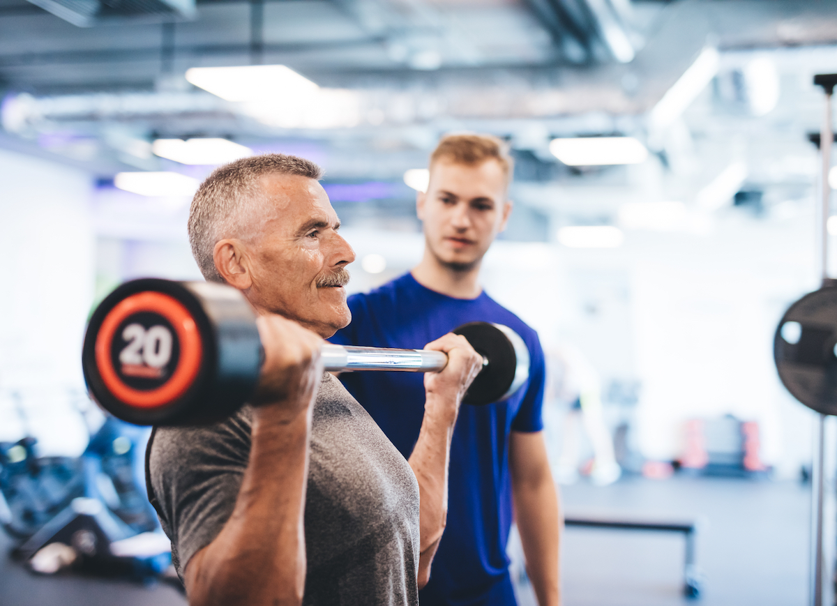 older man lifting weights at gym with spotter