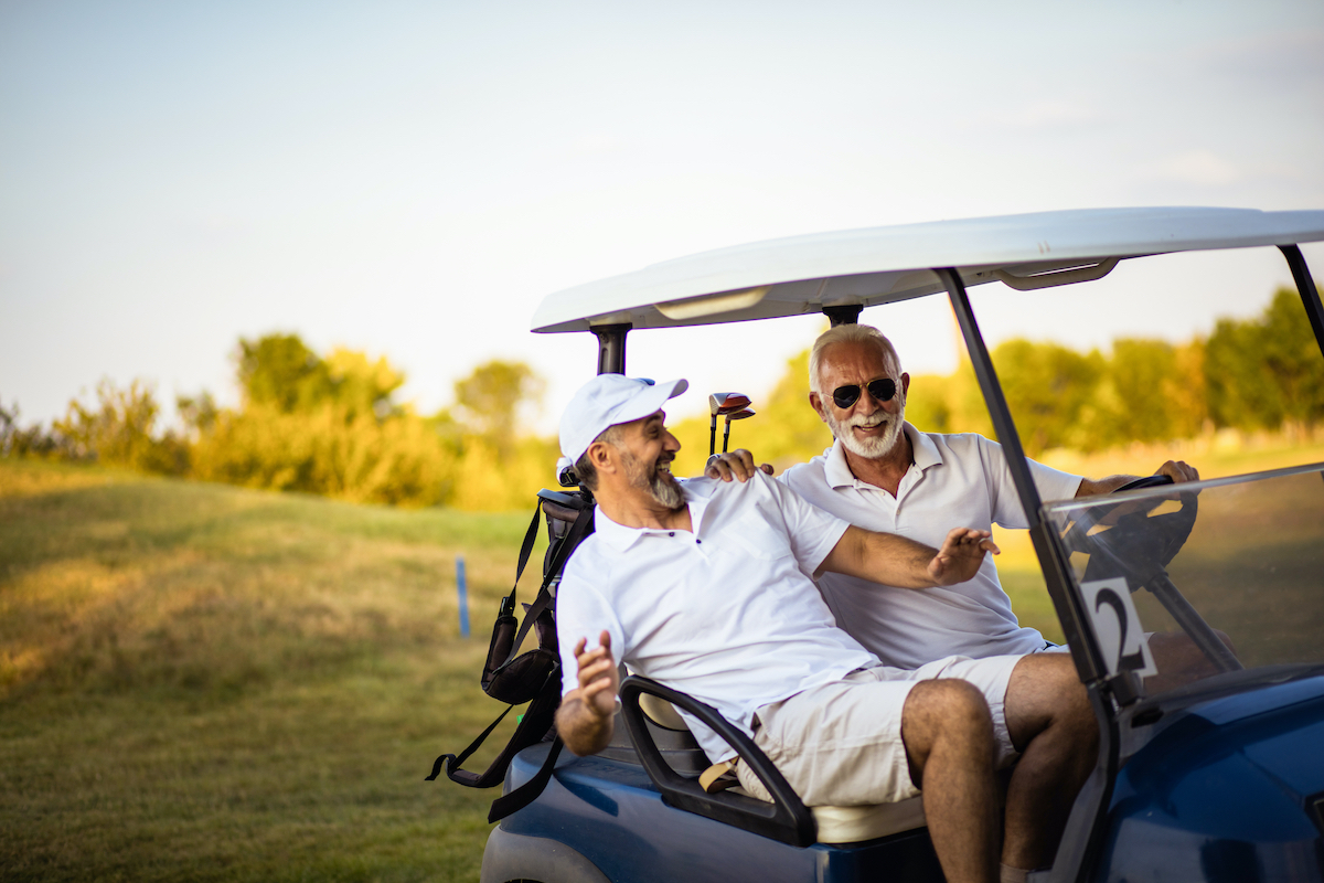 Two older friends are riding in a golf cart.