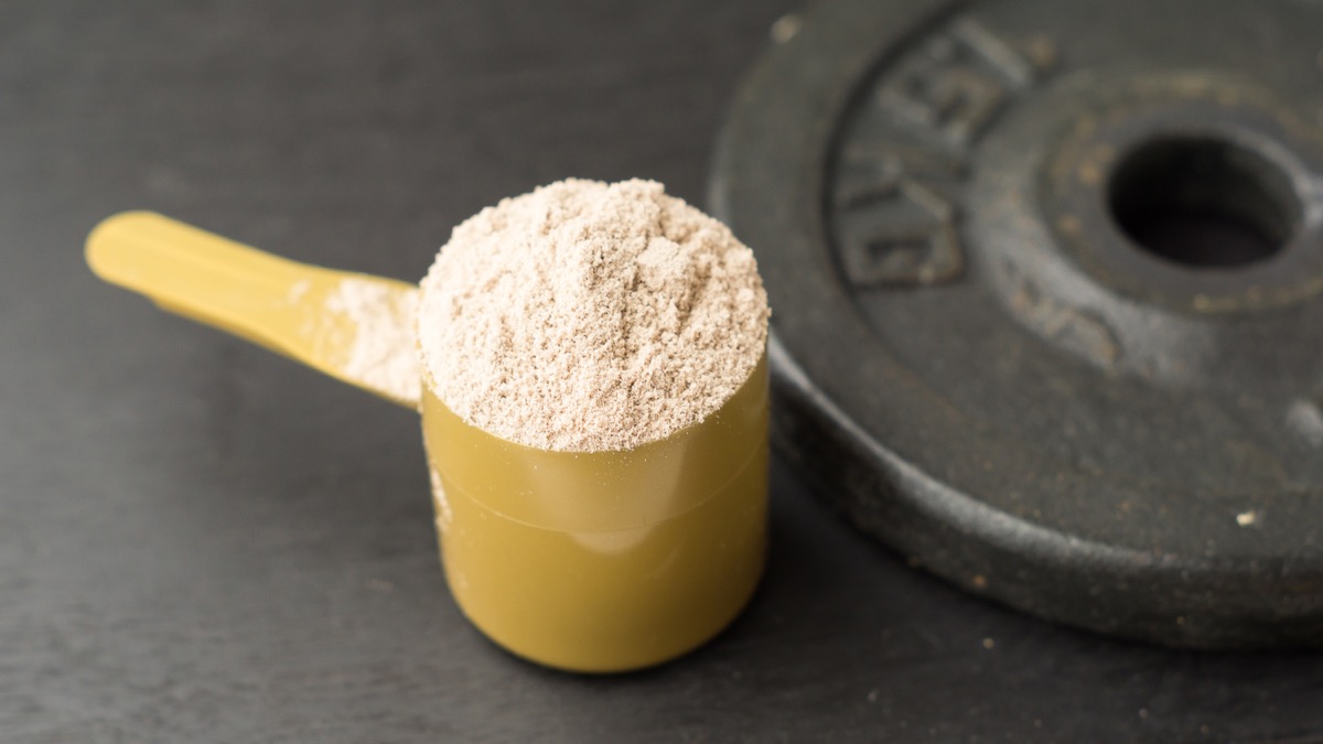 whey protein powder in yellow scoop next to weight plate
