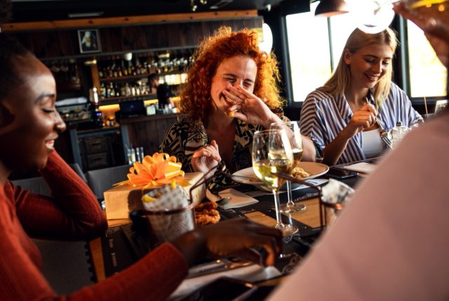 a woman with red curly hair laughs with her friends in a restaurant