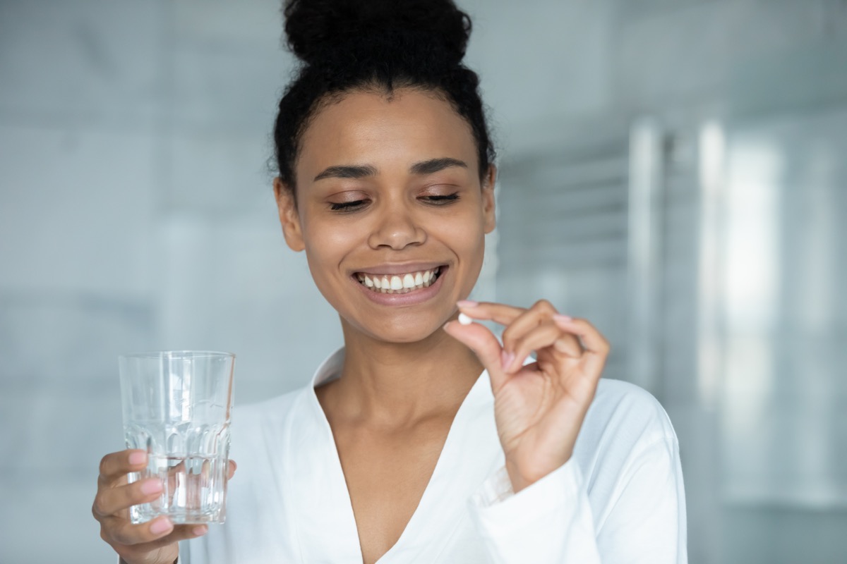 young woman in white shirt looking at pill and holding glass of water