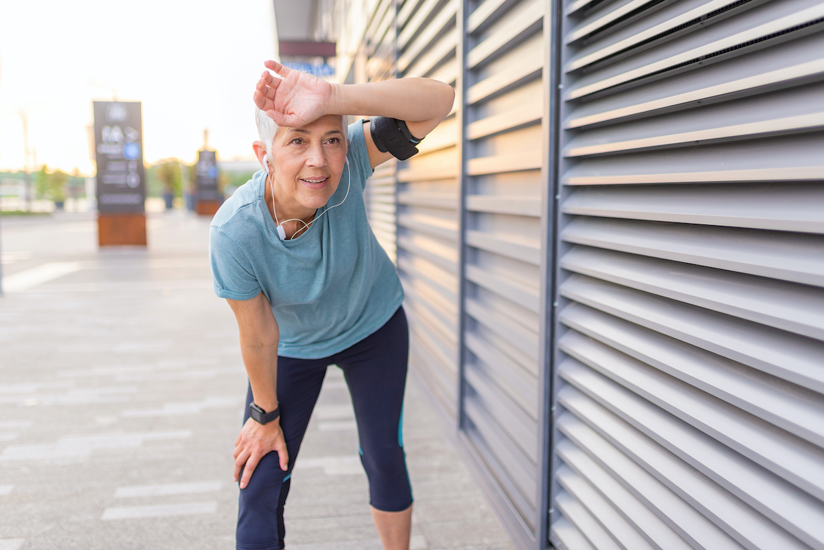 Tired senior woman after jogging. Tired senior woman resting after running outdoors. African female runner standing with hands on knees. Fitness sport woman resting after intensive evening run