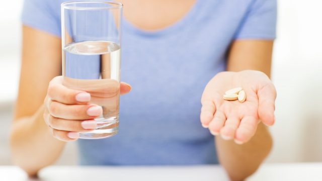woman in blue crew neck t-shirt holding glass of water and handful of supplements