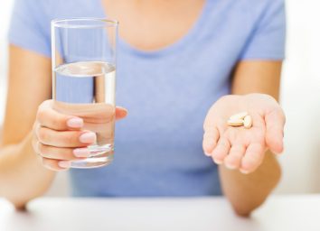 woman in blue crew neck t-shirt holding glass of water and handful of supplements