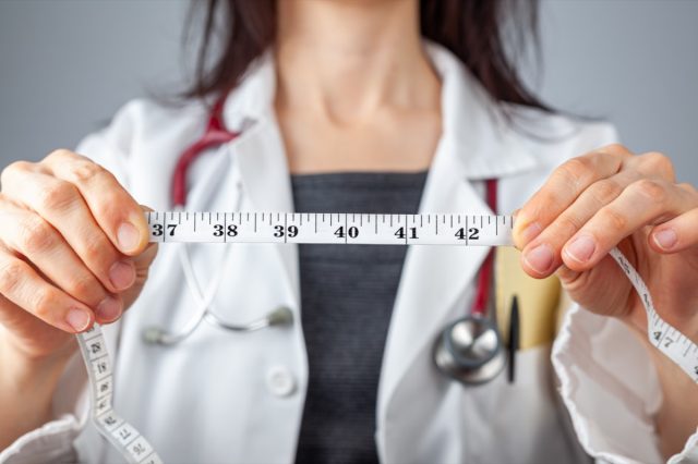 Doctor sosteniendo una cinta métrica en sus manos que muestra 40 pulgadas como circunferencia abdominal.