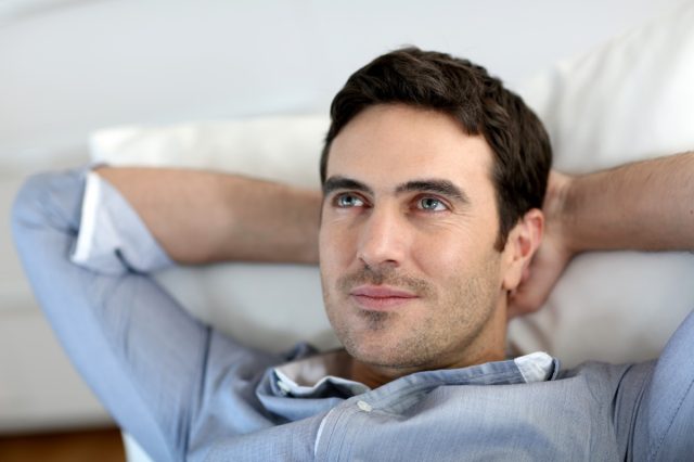 Man relaxing in sofa with arms behind head