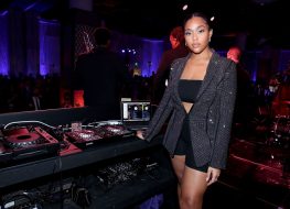 jordyn woods standing at dj booth in sparkly jacket, bandeau, and bike shorts