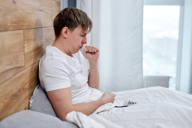 Man lying on bed at home, high fever and coughing.