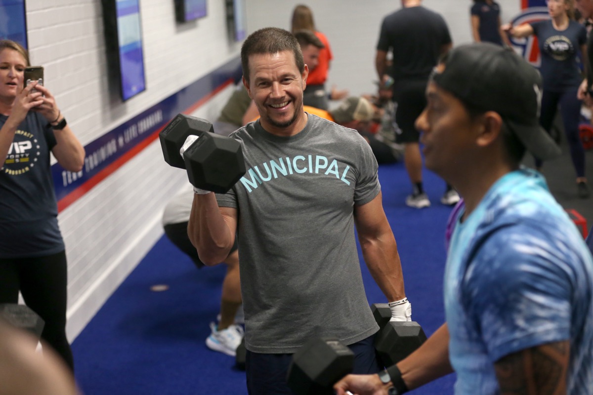 mark wahlberg doing dumbbell curls in a gym with other people