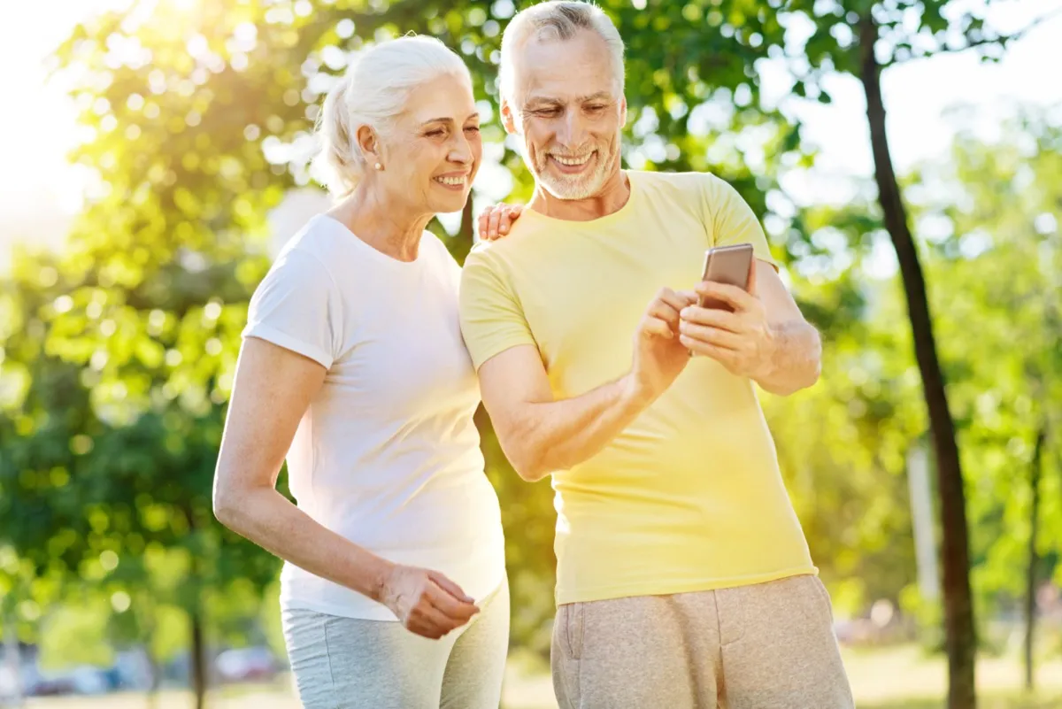 Happy mature couple looking at mobile phone in park.