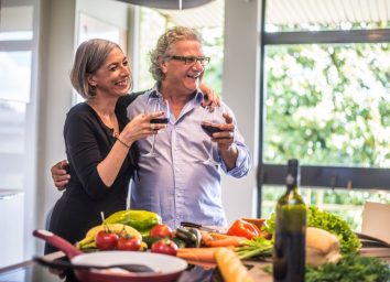 Senior couple cooking healthy food and drinking red wine at house kitchen.