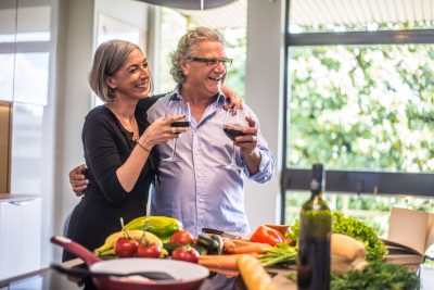 Senior couple cooking healthy food and drinking red wine at house kitchen.