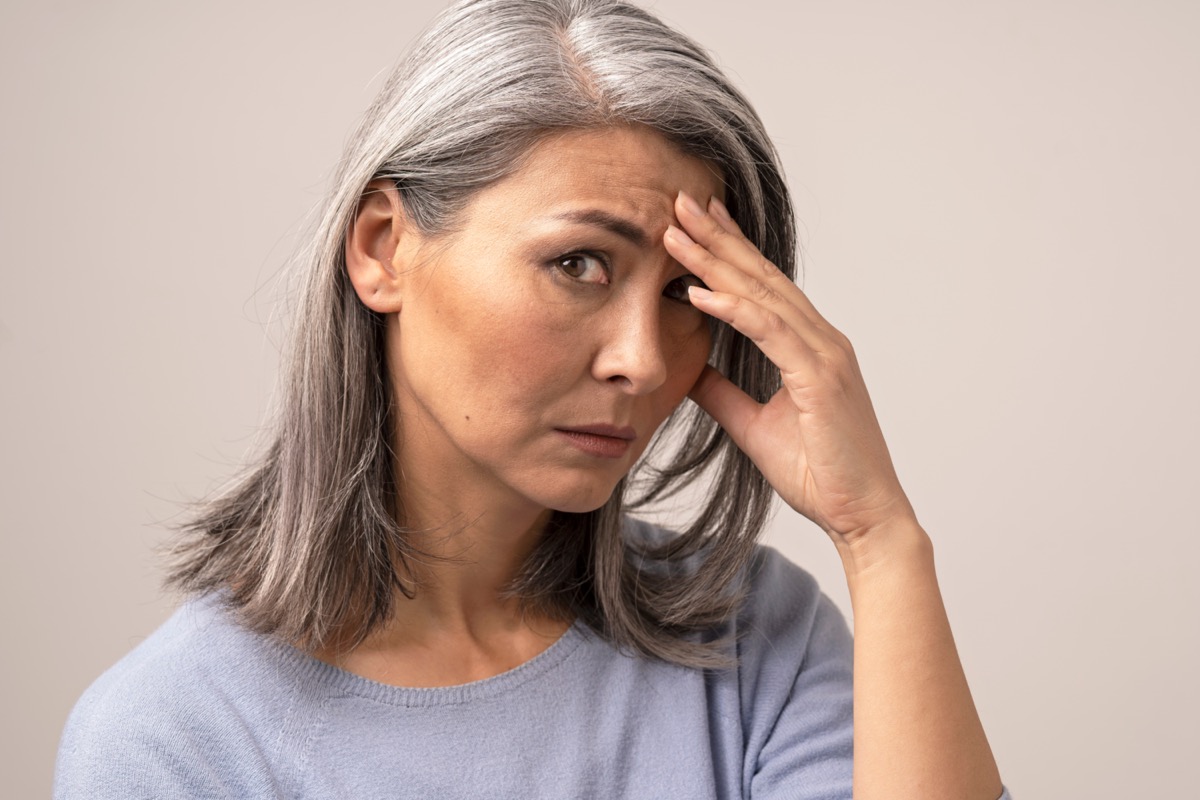 Sad mature woman puts her hand on her forehead.
