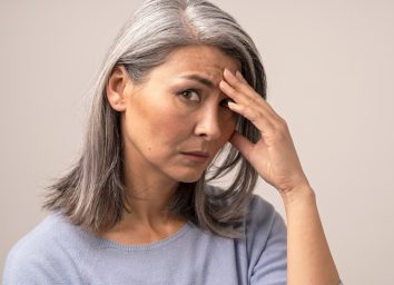 Sad mature woman puts her hand on her forehead.