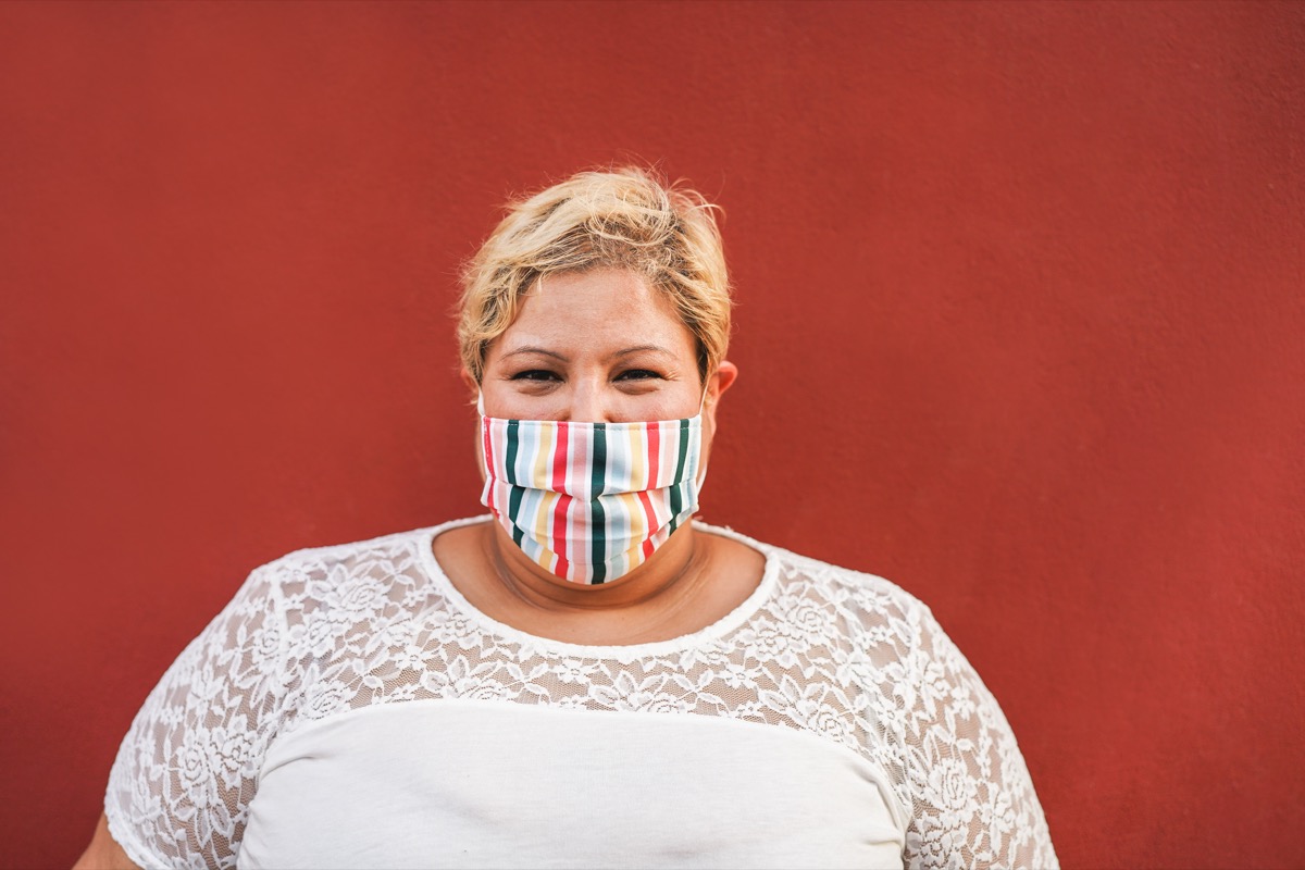 Curvy woman smiling on camera while wearing face protective mask outdoor