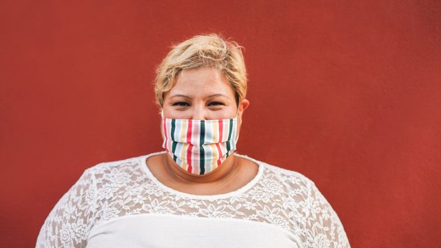 Curvy woman smiling on camera while wearing face protective mask outdoor
