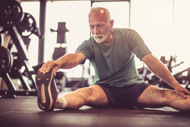 възрастен мъж, разтягащ се във фитнес зала