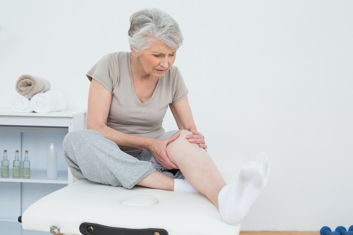 Senior woman with her hands on a painful knee while sitting on examination table