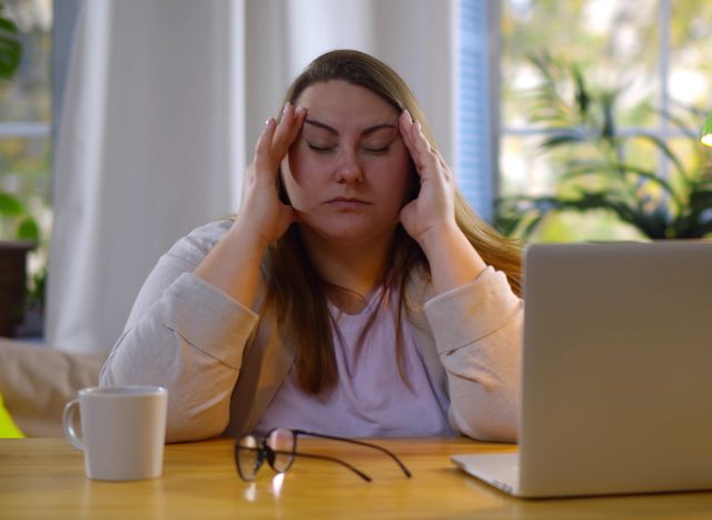 Tired overweight woman suffering eyestrain working on laptop at home