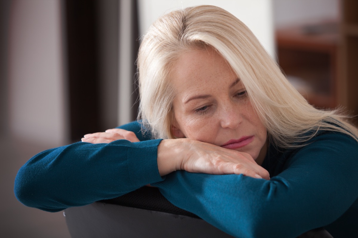 Sad depressed woman at home sitting on the couch, looking down and touching her forehead