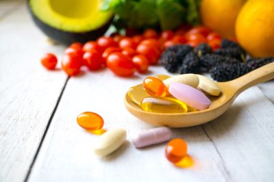 wooden spoon full of supplements with fruits and vegetables in the background