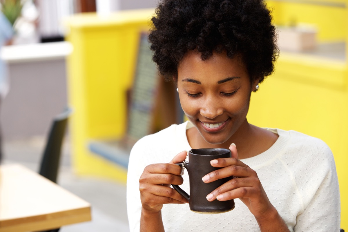 young woman with curly hair drinking from black mug