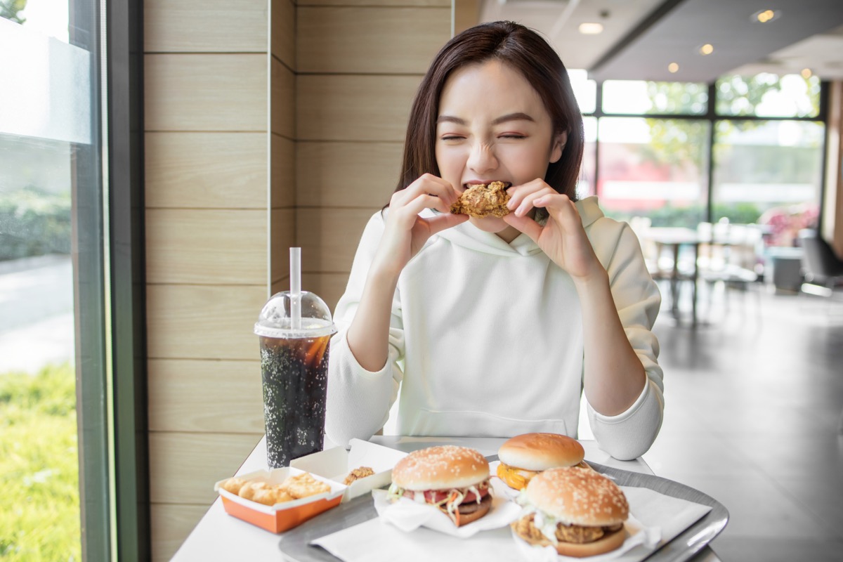 young woman eating chicken in fast food restaurant