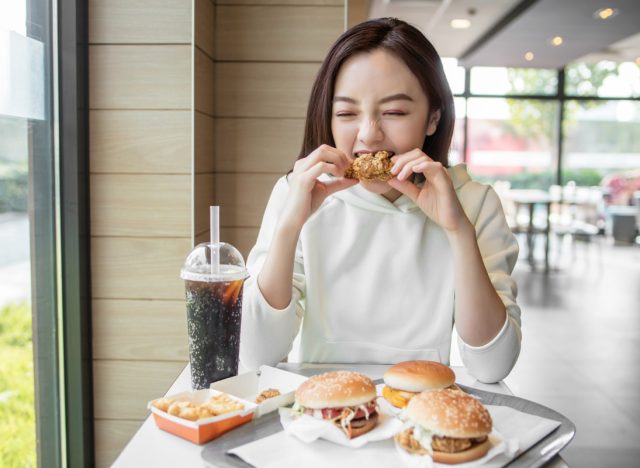 young woman eating chicken in fast food restaurant