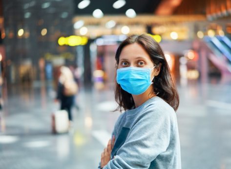 Traveler woman in virus protection face mask in international airport.