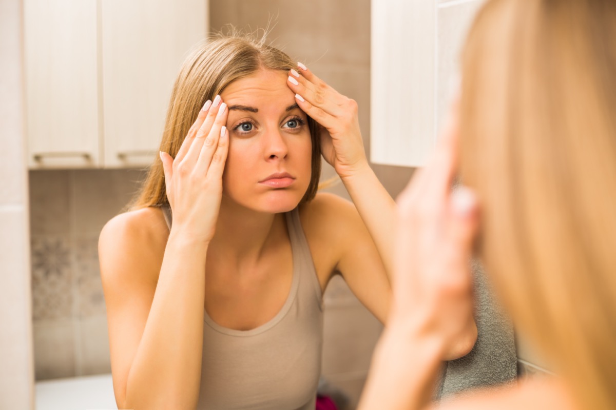 Worried woman is looking her wrinkles in the bathroom.