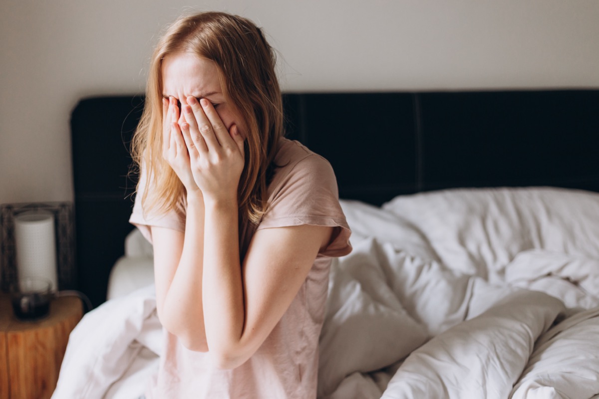 Woman sitting on bed and holding head in her hands.
