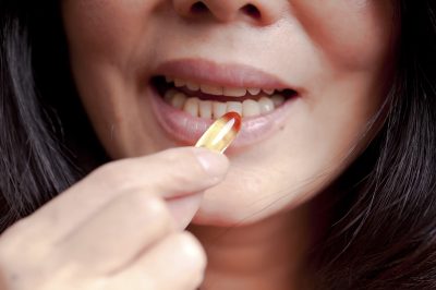 middle aged woman with dark hair taking fish oil supplement