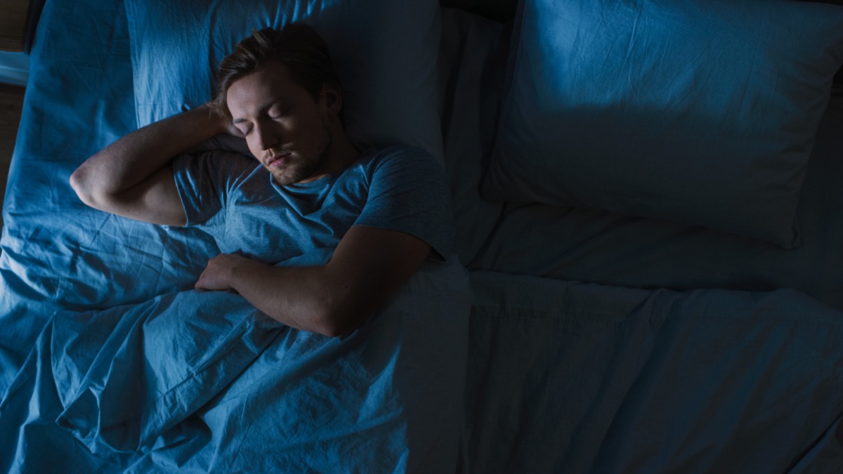 young blond man sleeping in bed at night