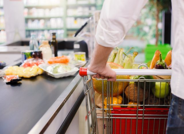 man in white shirt pushing cart through grocery store checkout lane